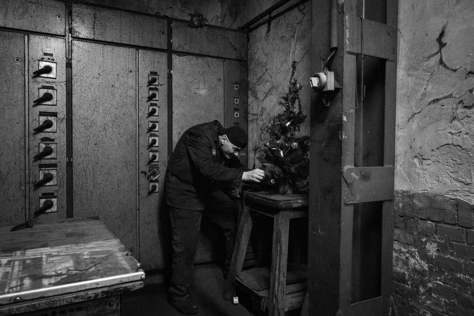Trabajador ferroviario manipula un pequeño árbol de Navidad dentro de un antiguo taller con paneles eléctricos.