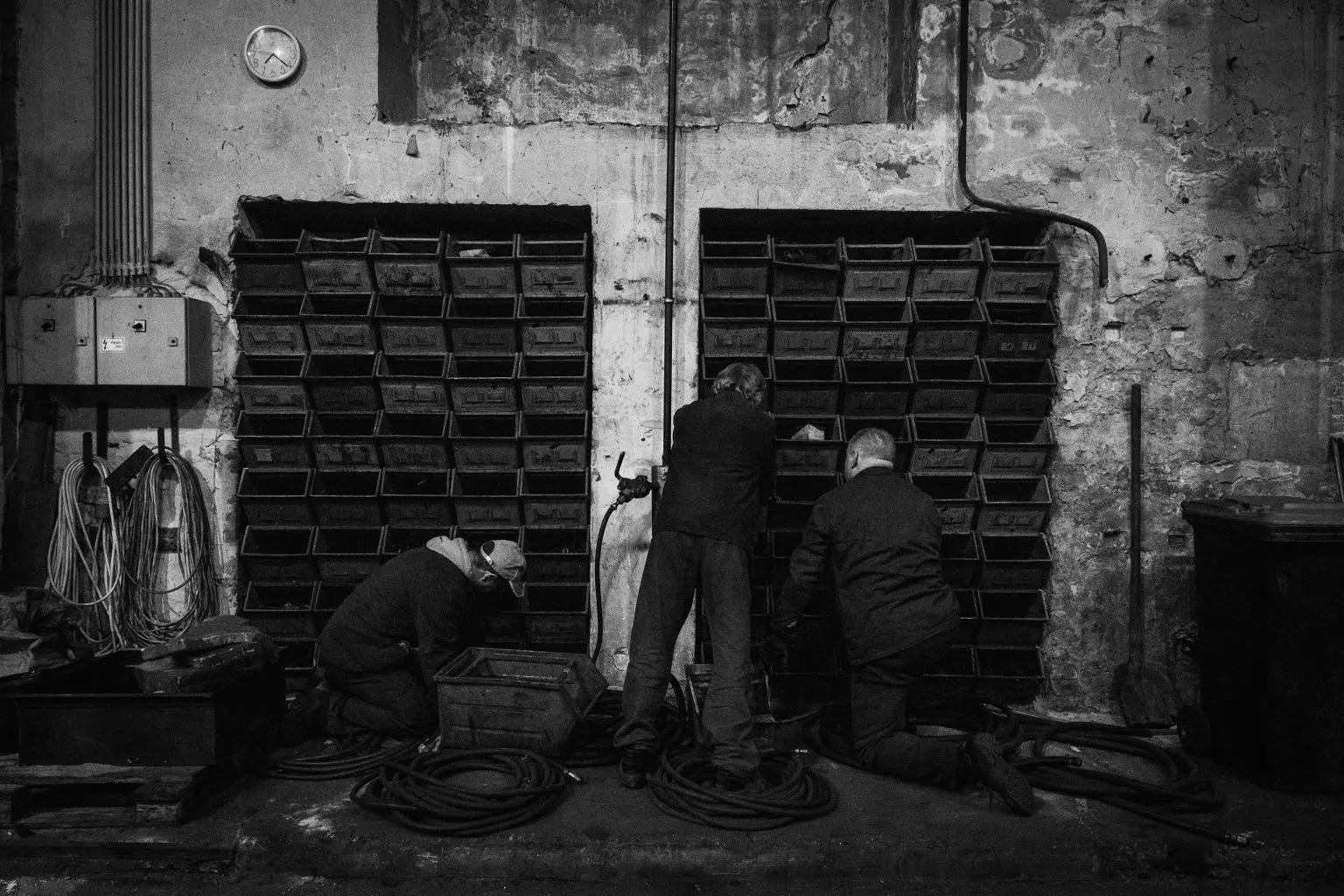 Tres trabajadores revisan piezas y herramientas frente a estanterías dentro de un antiguo taller ferroviario.