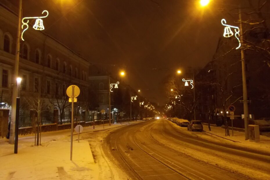 Calle Böszörményi de Budapest cubierta de nieve, con luces navideñas encendidas de noche.