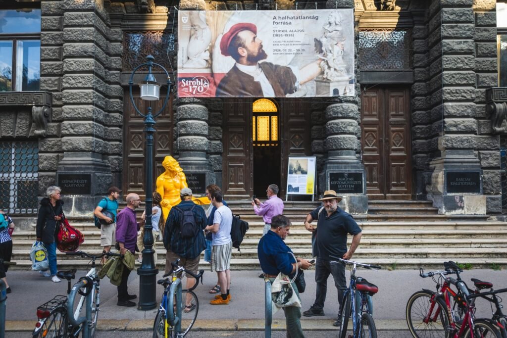 Entrada de la Universidad Húngara de Bellas Artes con la exposición Stróbl 170 y la figura dorada de Mihály