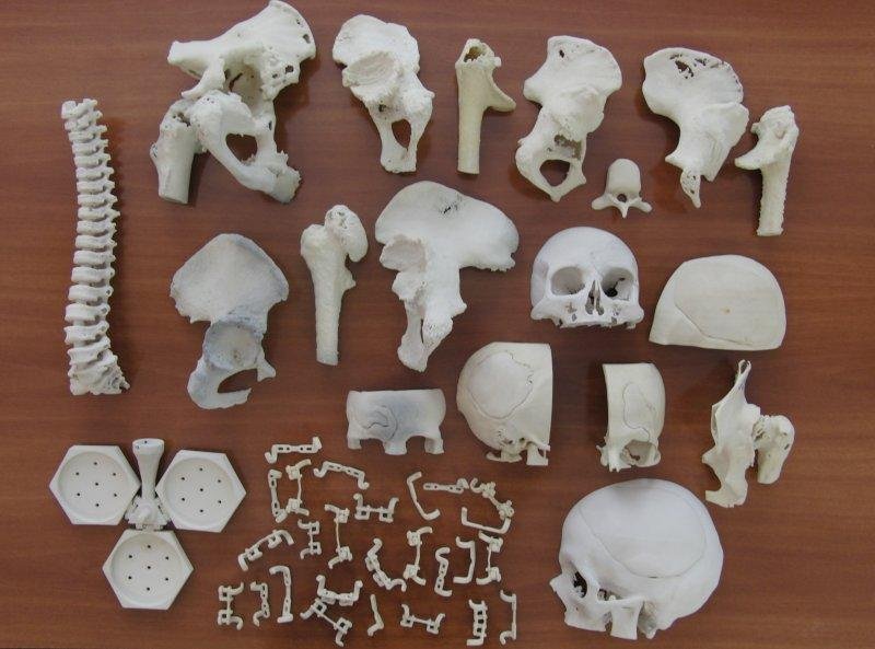 Colección de reproducciones anatómicas impresas en 3D, incluidos cráneos, vértebras, huesos y componentes óseos dispuestos sobre una mesa.