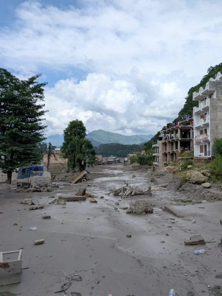 Una calle de Rasuwa cubierta de barro y escombros, con vehículos atrapados y edificios afectados tras la riada de agosto de 2026.