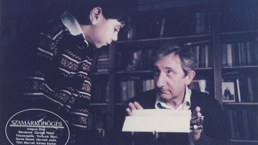 Escena de Szamárköhögés: un niño junto a un hombre con una máquina de escribir.